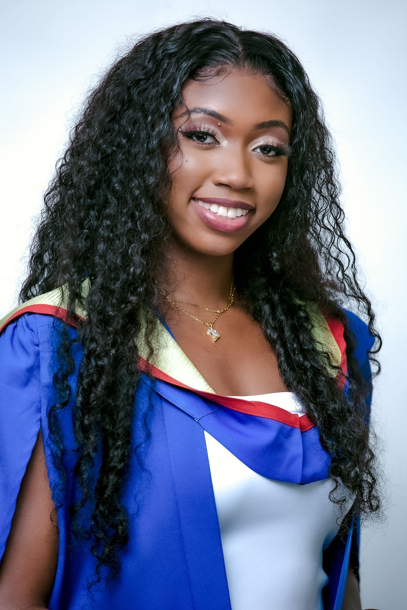 Graduate portrait in blue academic regalia with long curly hair against light background.