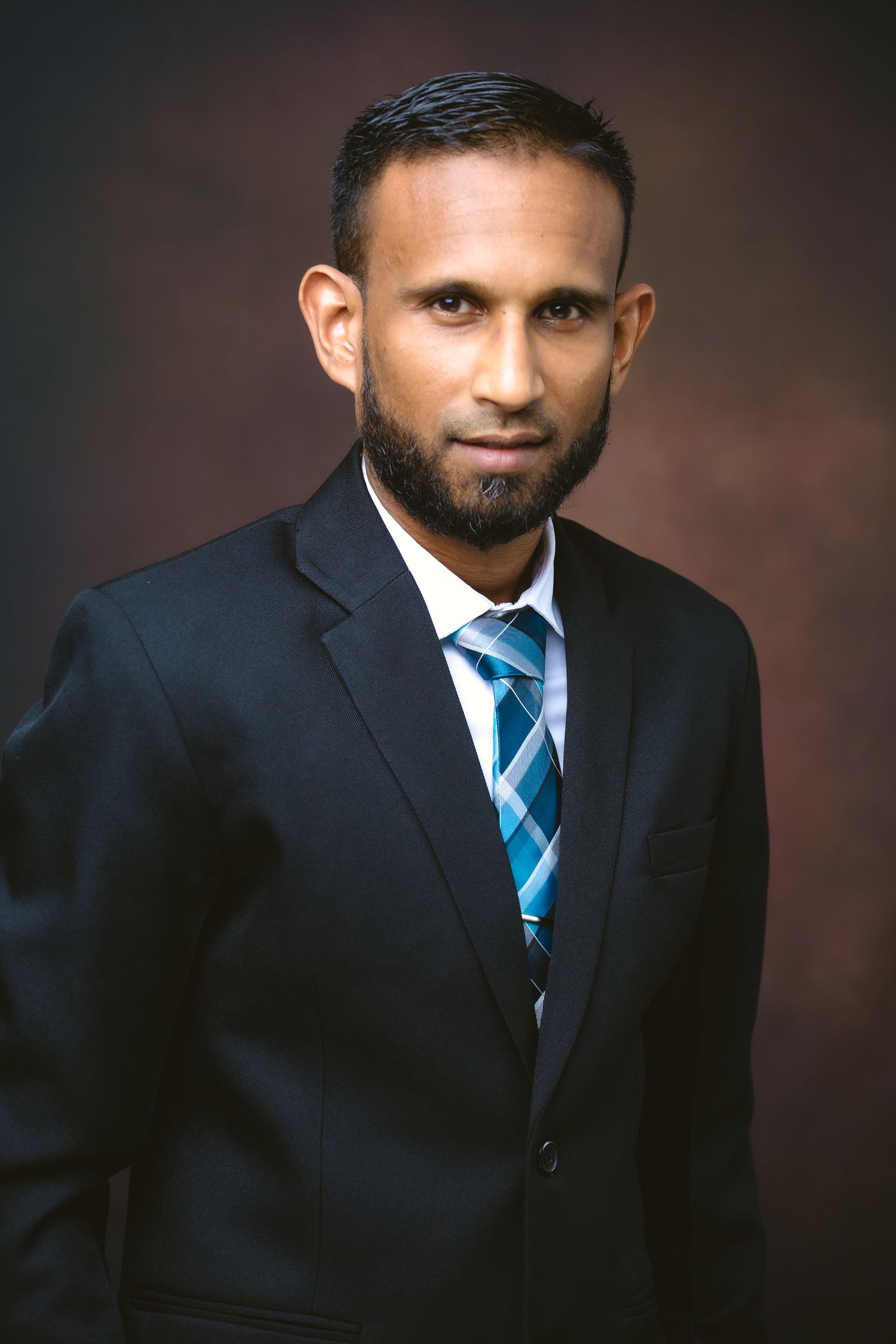 Professional headshot portraits in formal black suit and blue striped tie against dark background.