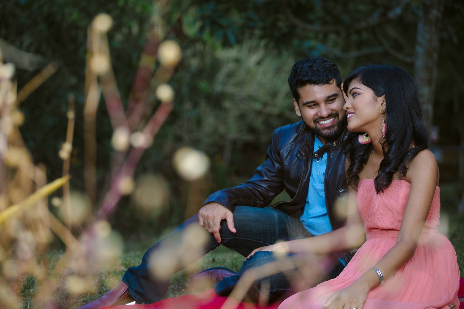 A couple sitting together outdoors share a romantic moment in soft lighting with person in pink dress and blue jacket.