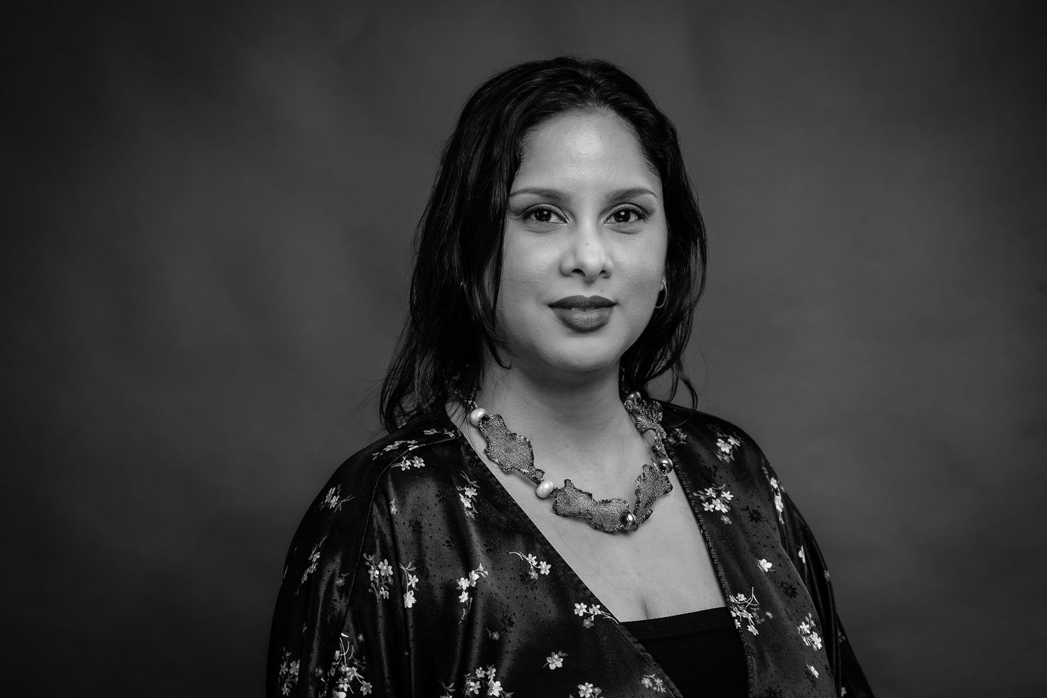 Black and white studio portrait of a person wearing a patterned dress and statement necklace.