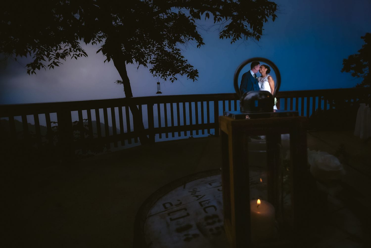 A beautiful Bride and Groom, against a blue twilight sky on a deck with glowing candlelight below. Captured at North Deck, Maracas Trinidad
