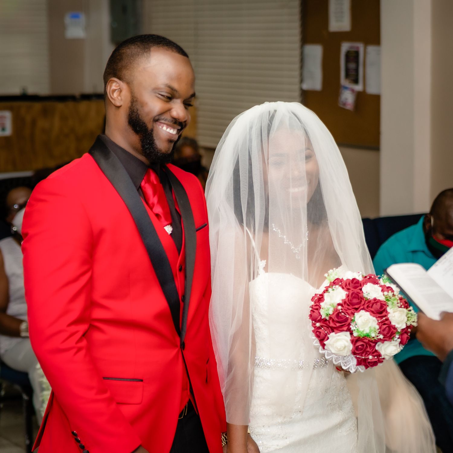 A wedding couple shares a joyful moment, with the groom in a striking red suit jacket.