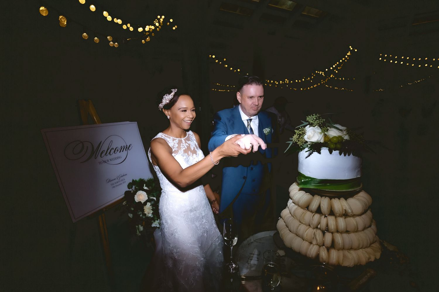 Newlyweds cutting their wedding cake decorated with cookies at evening reception.