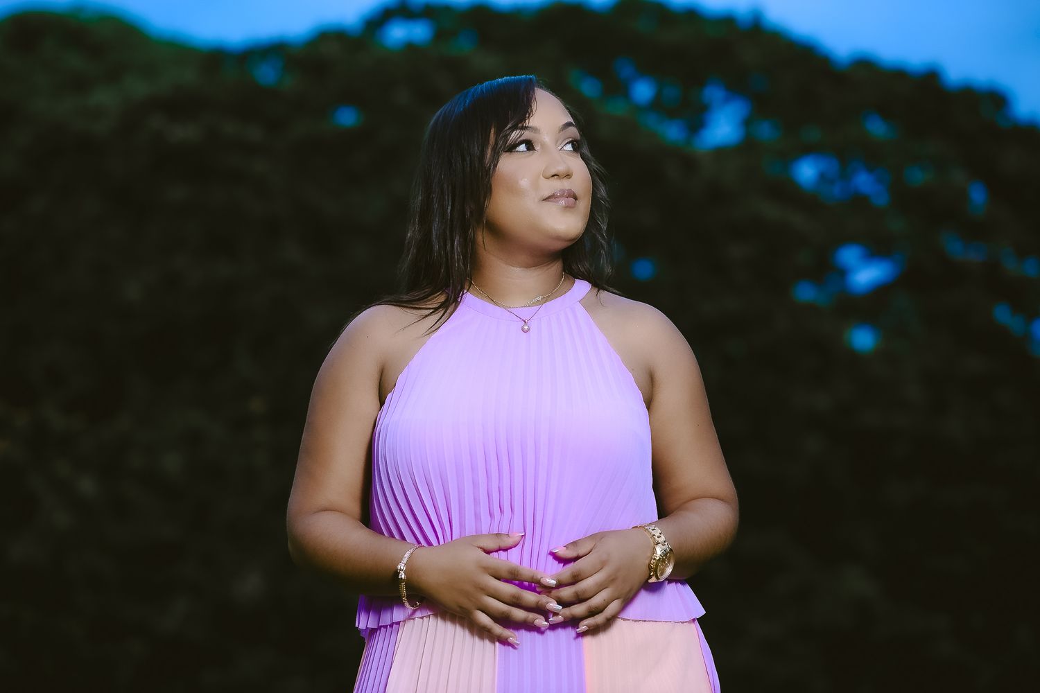 Woman in purple halter dress poses against twilight sky.