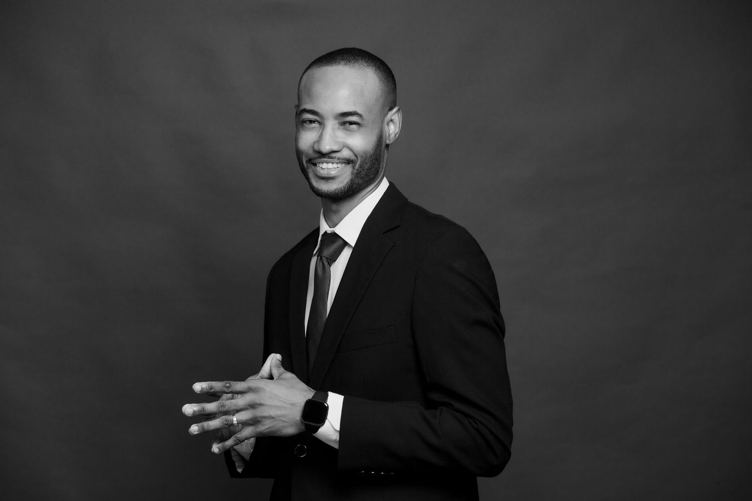 Black and white studio portrait of person in suit with animated hand gesture.