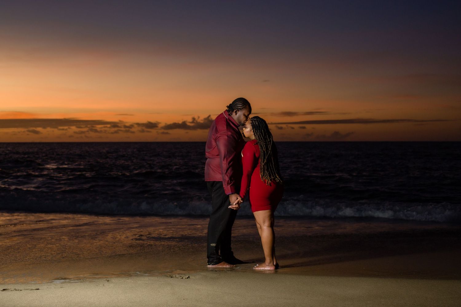 Romantic couple embracing on beach at sunset with dramatic orange sky.
