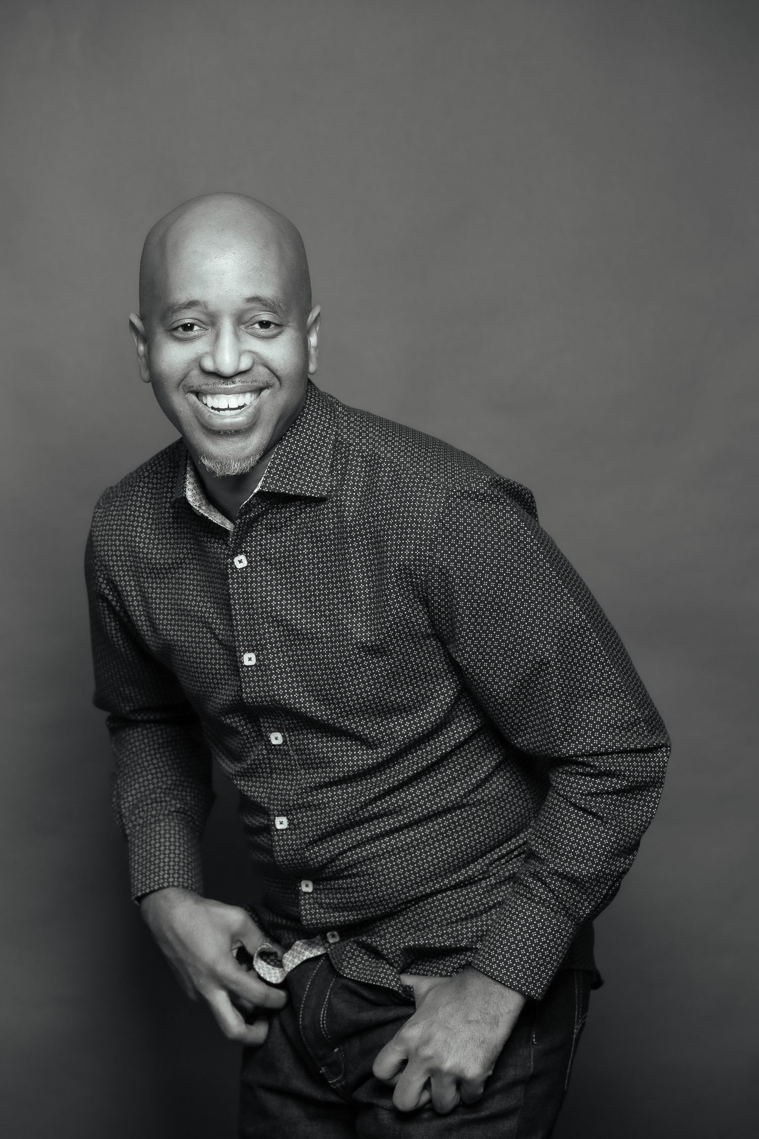 A black and white studio portrait of a person in business attire smiling warmly.
