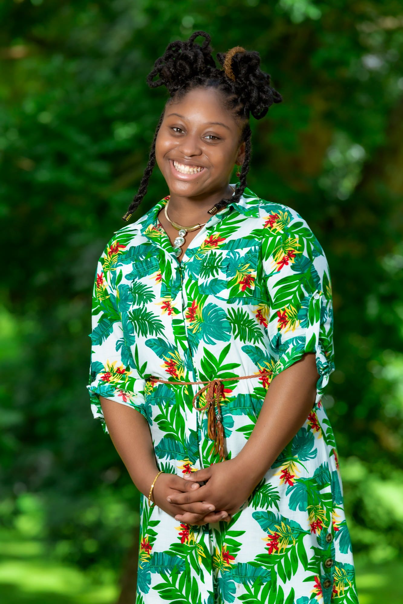 Person wearing vibrant tropical print dress poses outdoors in lush green setting.