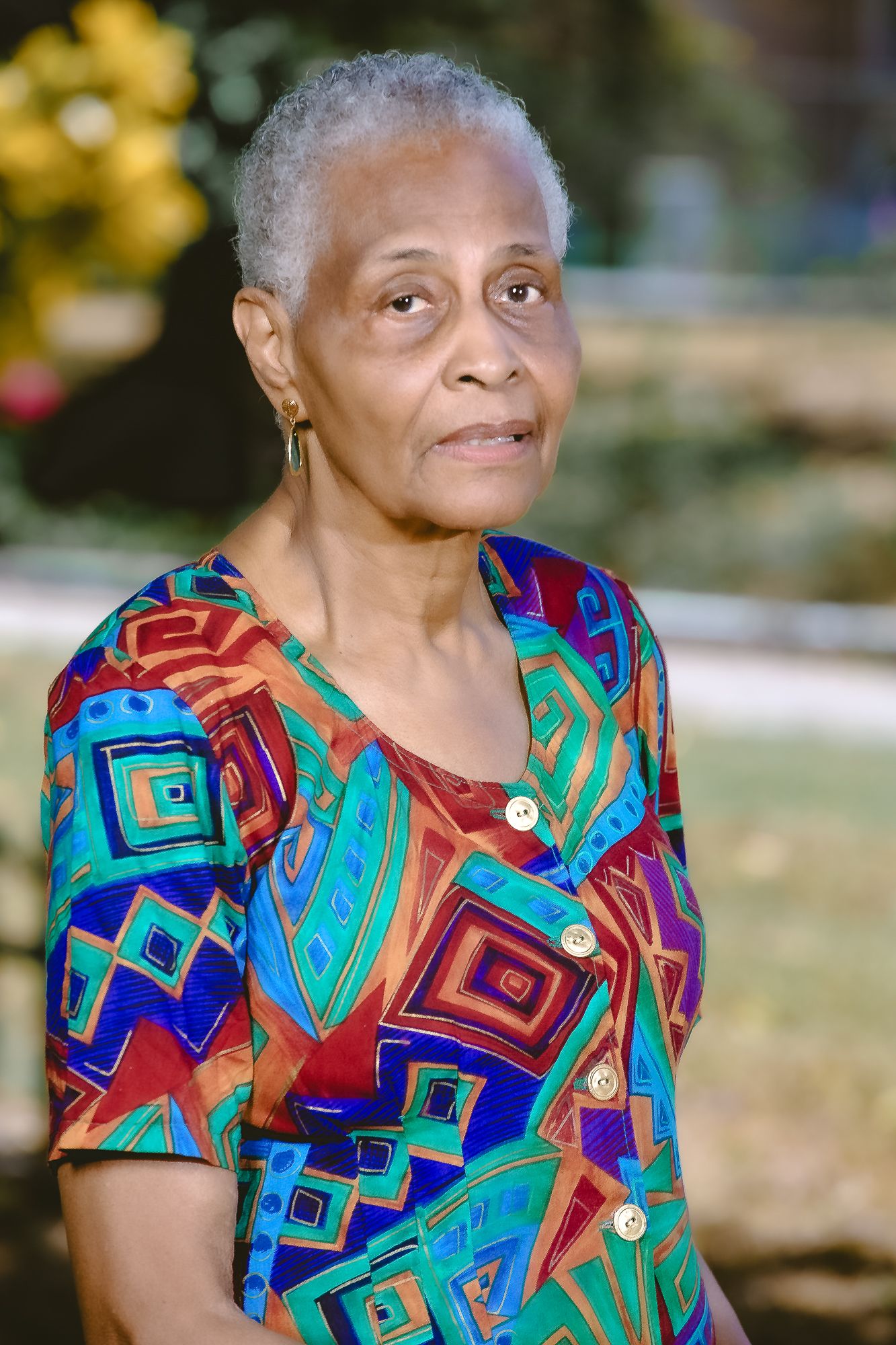 Portrait wearing colorful geometric print top in outdoor garden setting.