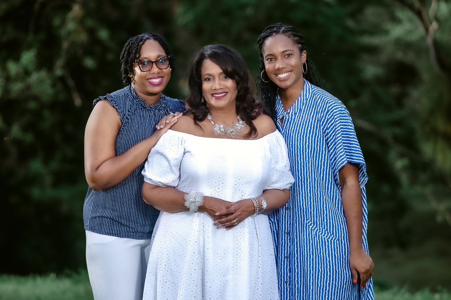 Three people in coordinating blue and white outfits pose together outdoors for a casual family portrait.
