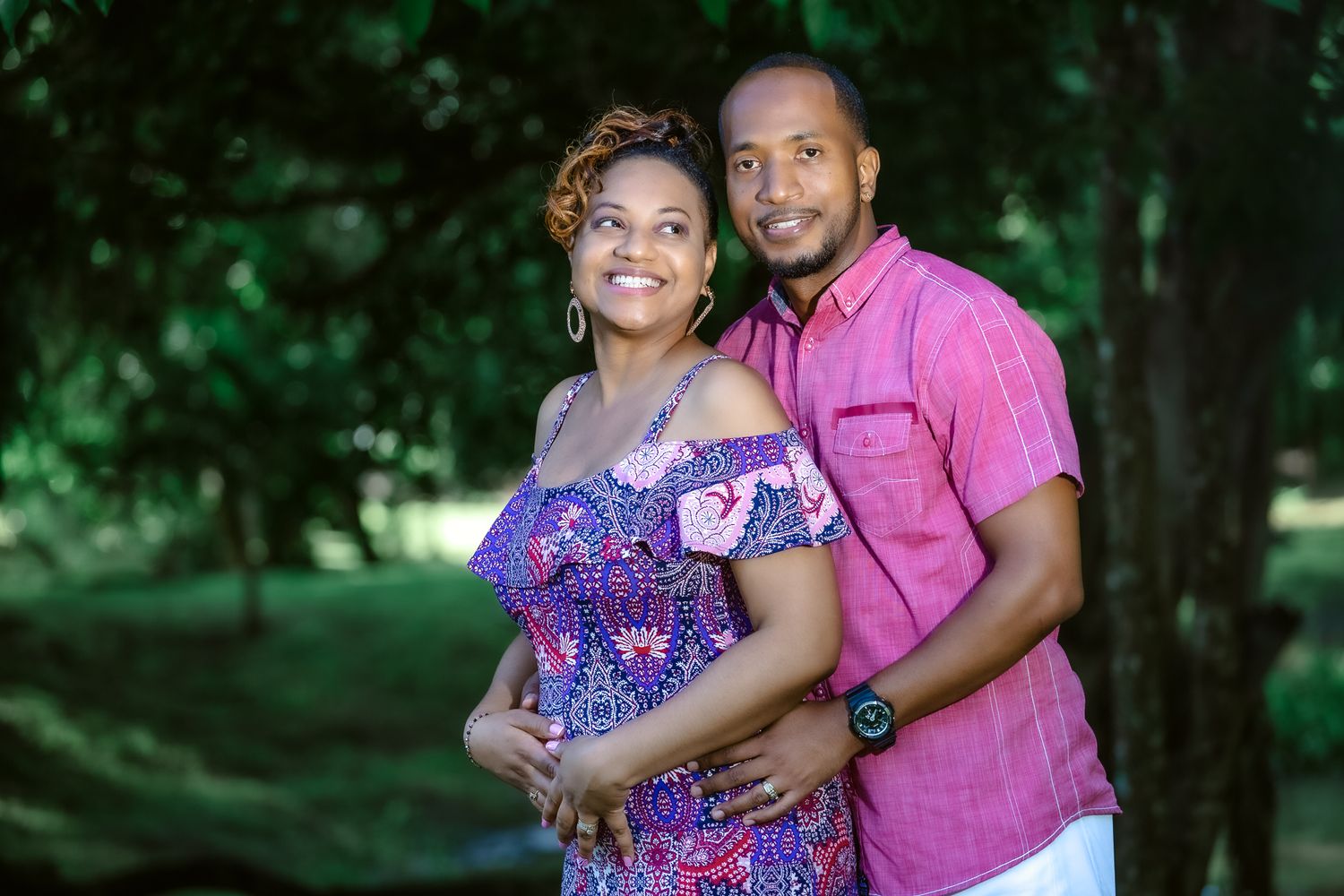 A couple poses together outdoors, wearing colorful outfits against a backdrop of trees.