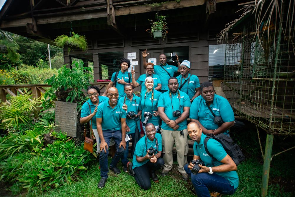 A group wearing matching teal shirts poses together during a team building activity or volunteer event outdoors.