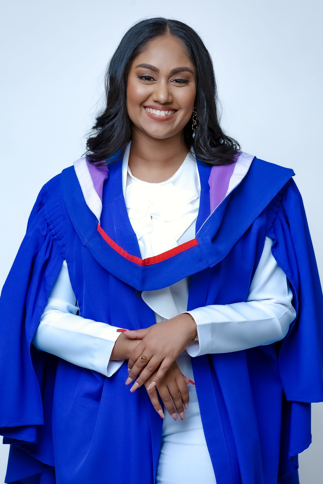 Graduate wearing blue academic regalia with hood and white dress smiles at camera during graduation photo session.