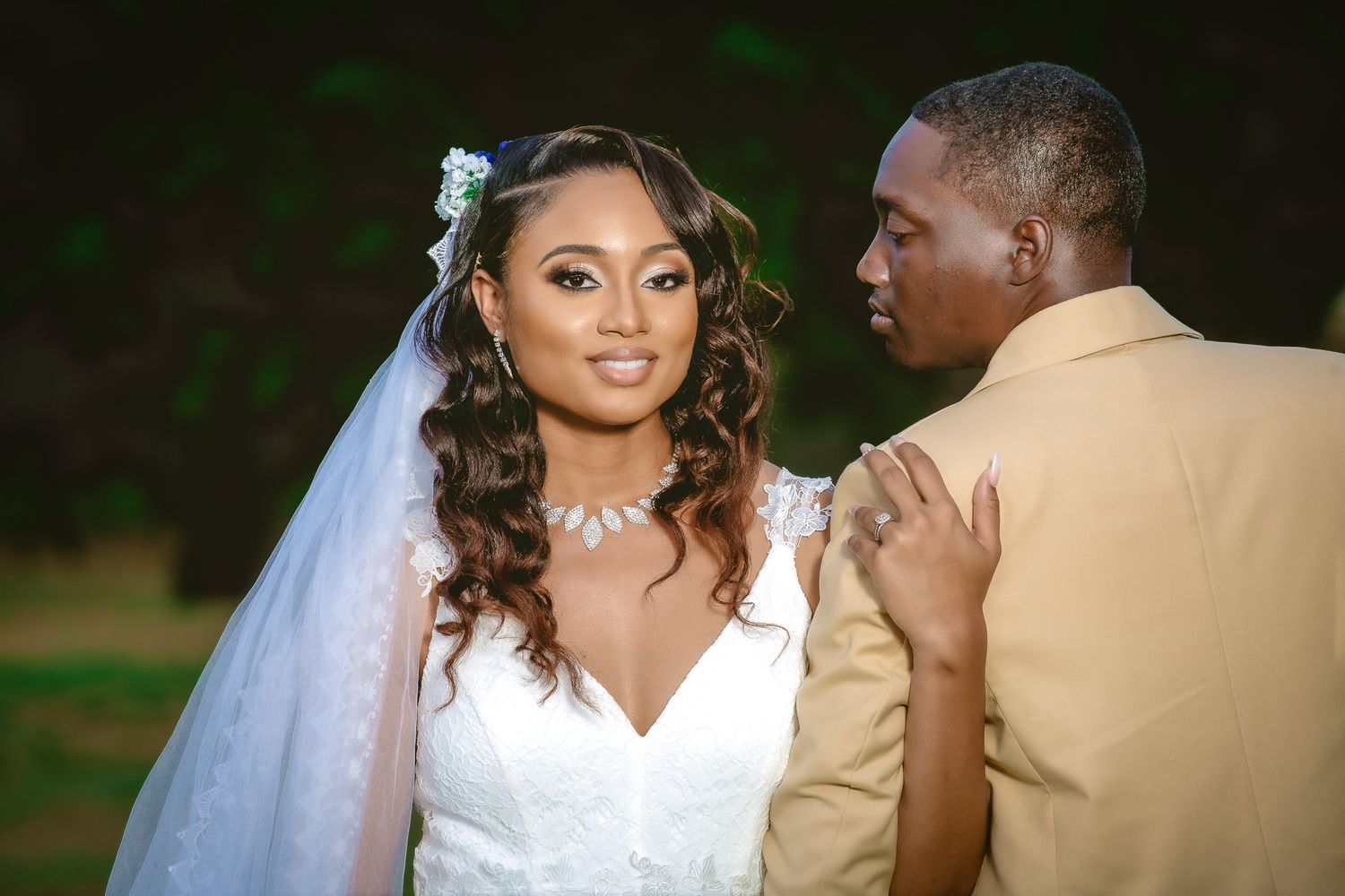 Bride in elegant white gown and veil shares a tender moment with groom in tan suit.