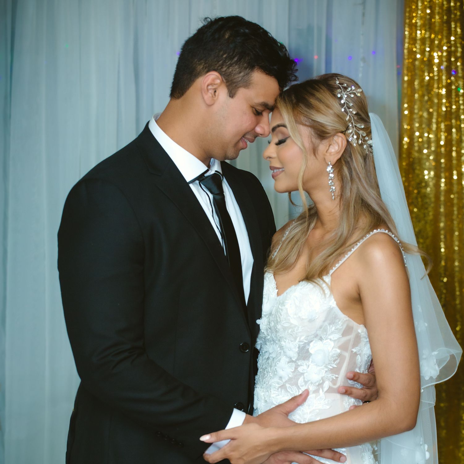 Romantic wedding portrait against gold sequin backdrop with soft lighting.