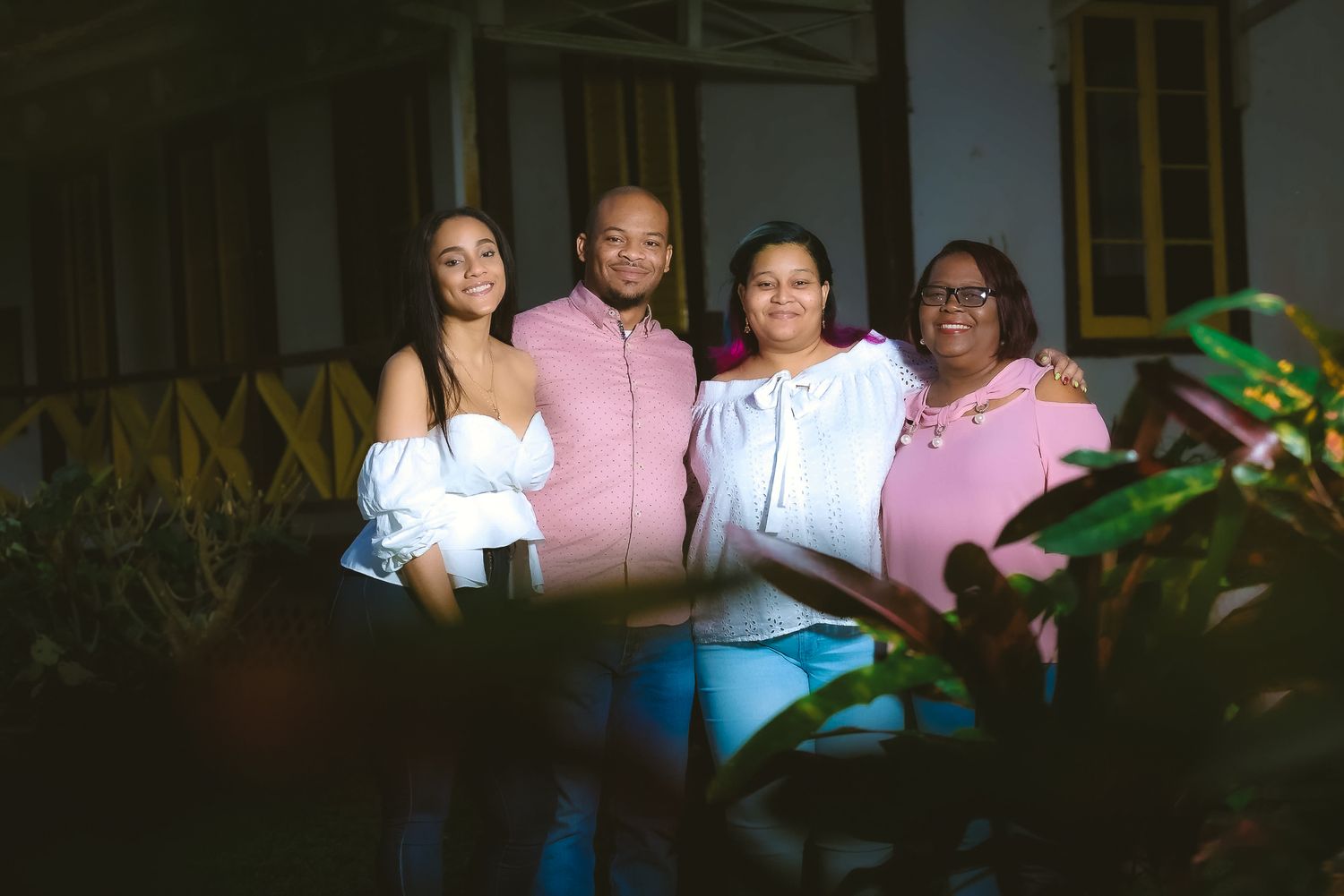 Group photo of four people wearing pink and white outfits on a porch at dusk.