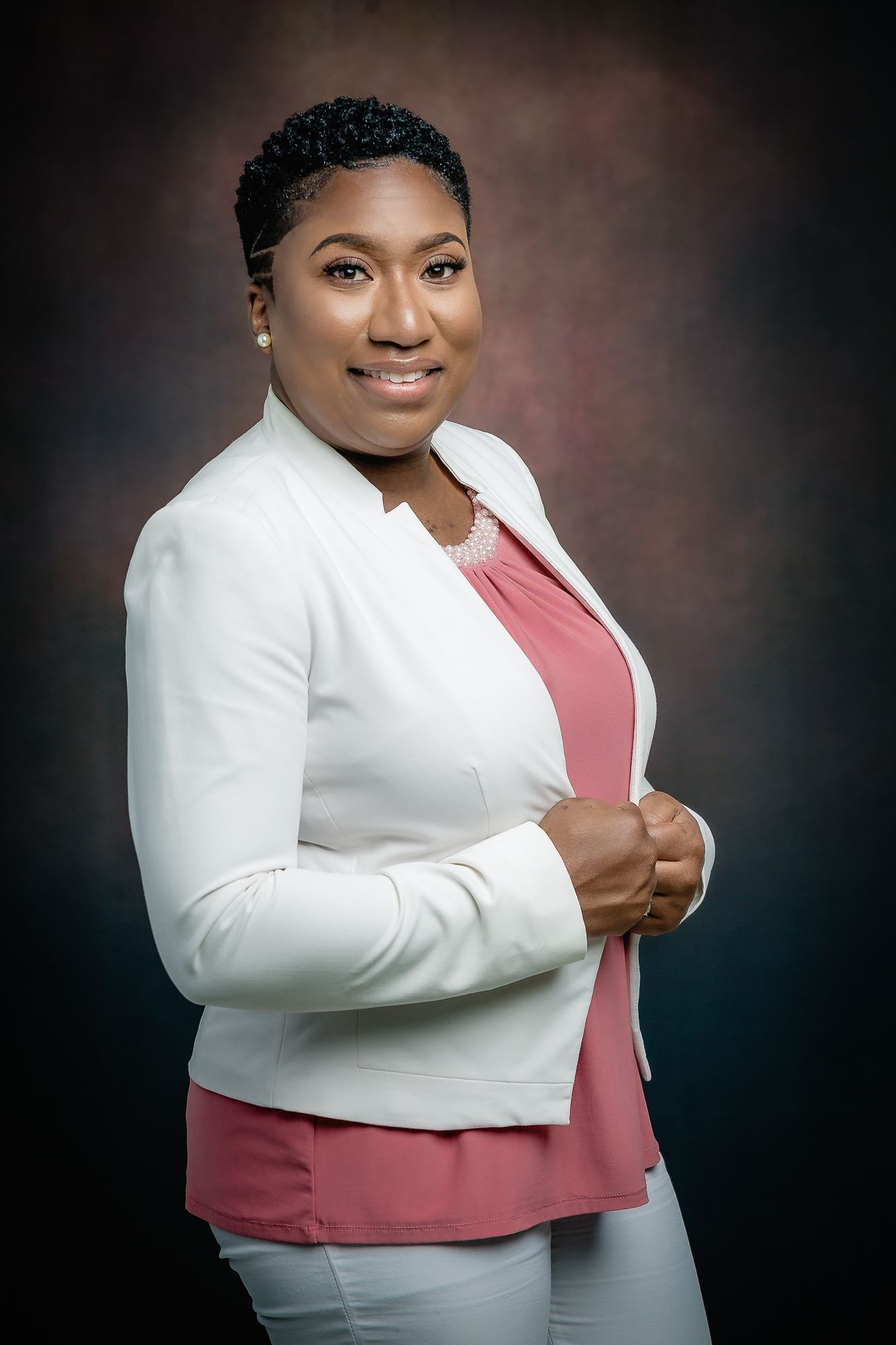 Professional headshot featuring white blazer and pink top with confident pose.