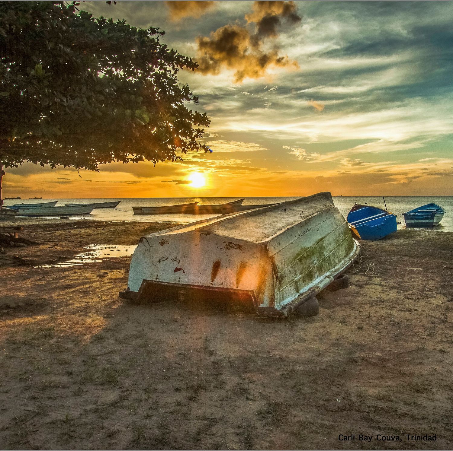 Abandoned boats on a sandy beach at sunset with dramatic orange and teal sky over the ocean.