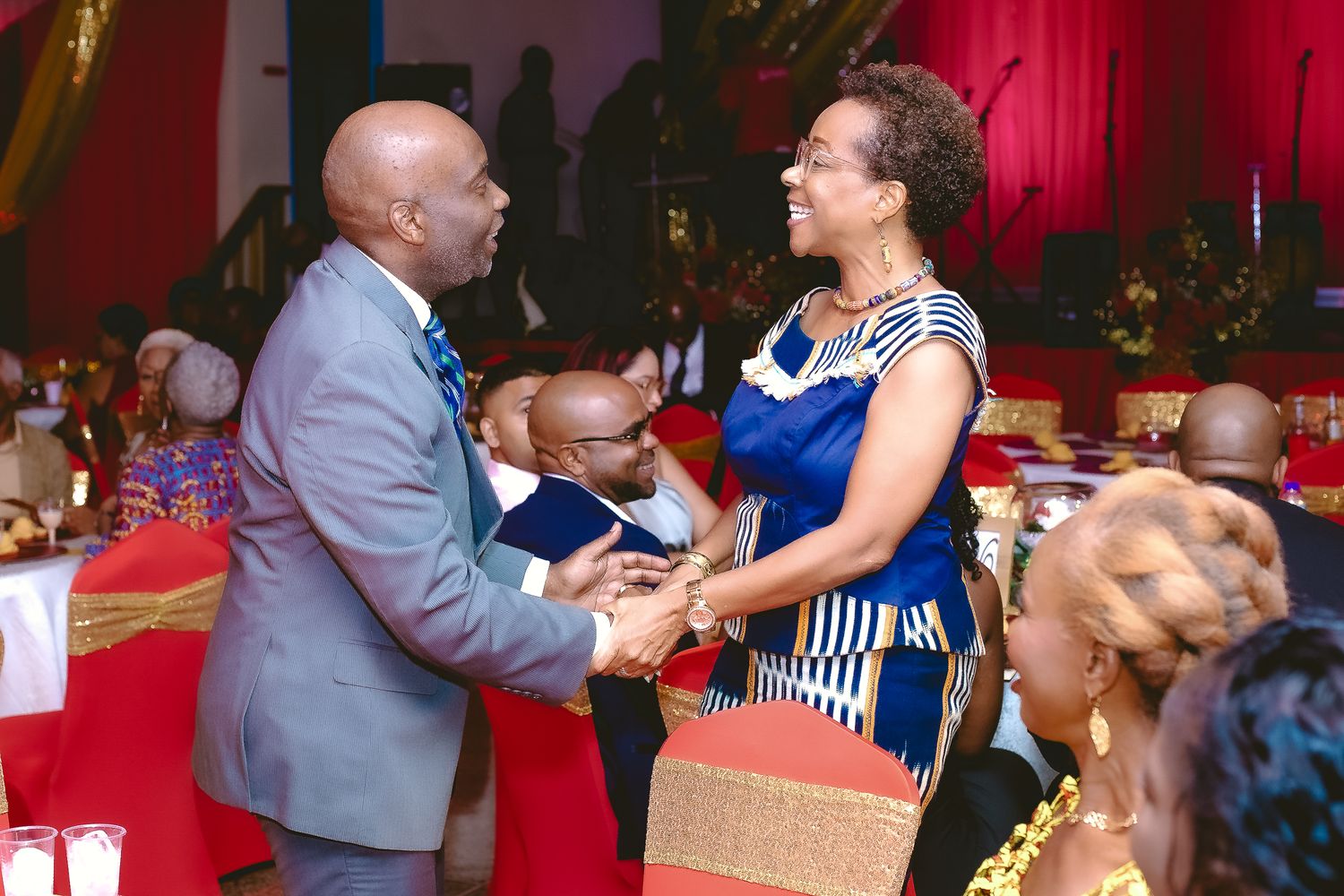 People interacting at a formal event with red curtains and decorative elements in background.
