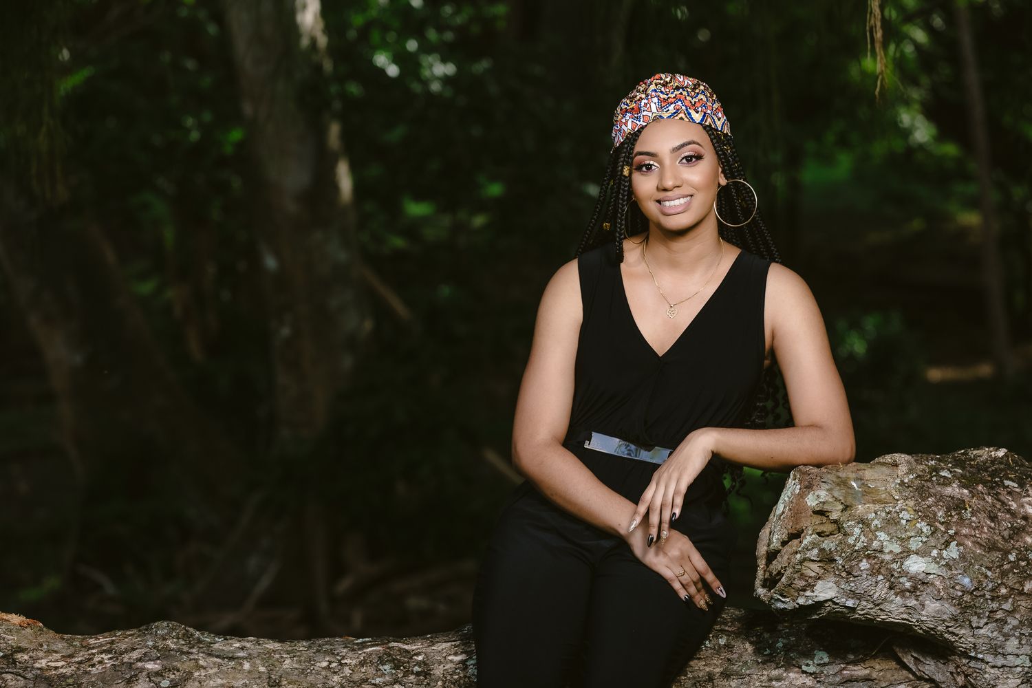 Person in black dress poses on rocky outcrop in forest setting.