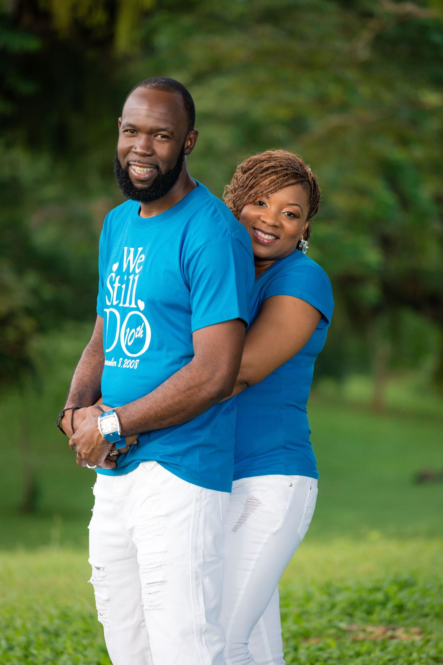 Couple in matching blue shirts and white pants pose together outdoors.