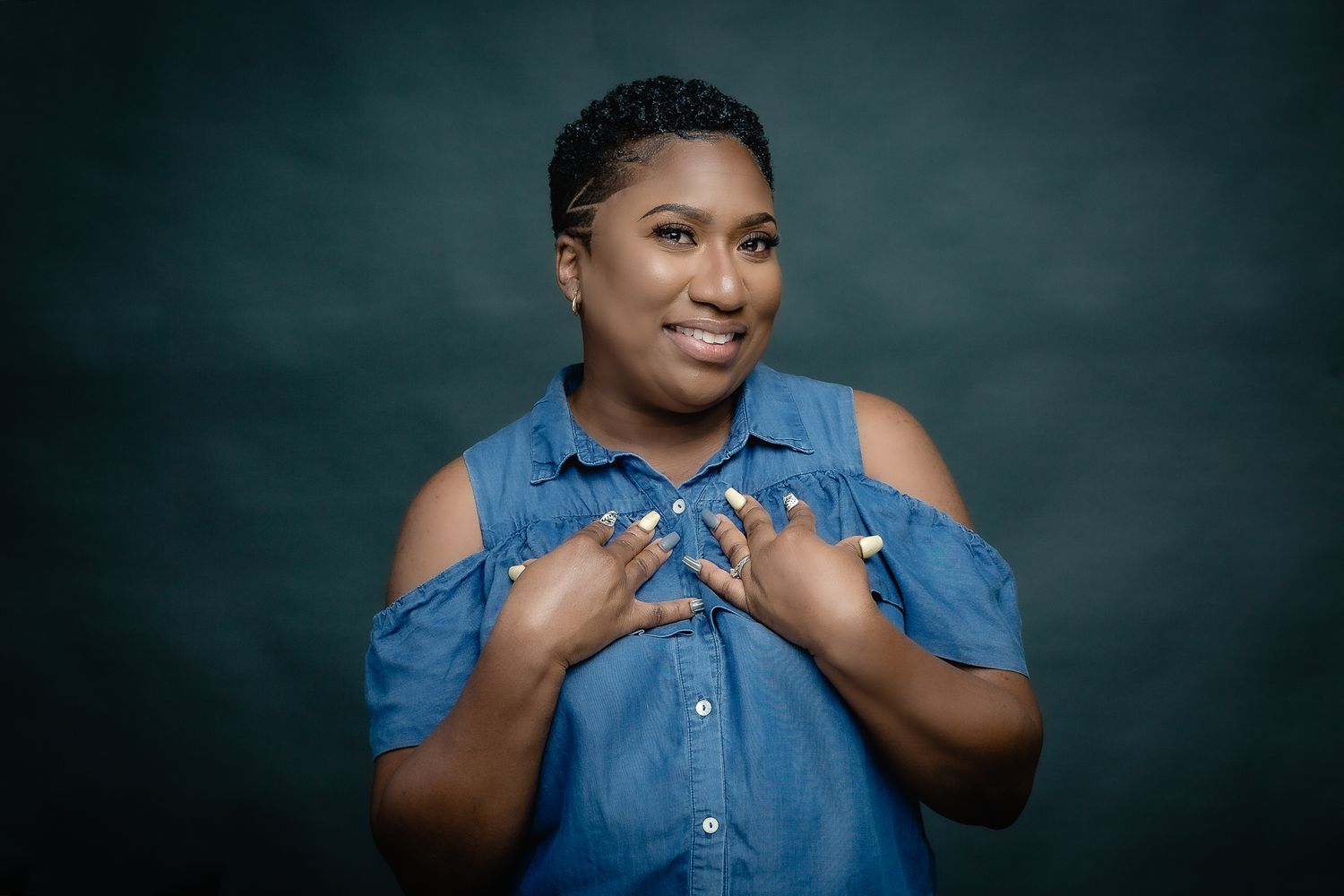Portrait in blue denim cold-shoulder top with joyful expression against dark backdrop.