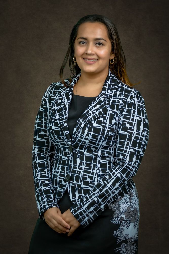 A person wearing a black and white patterned blazer poses against a dark background in a professional portrait series.