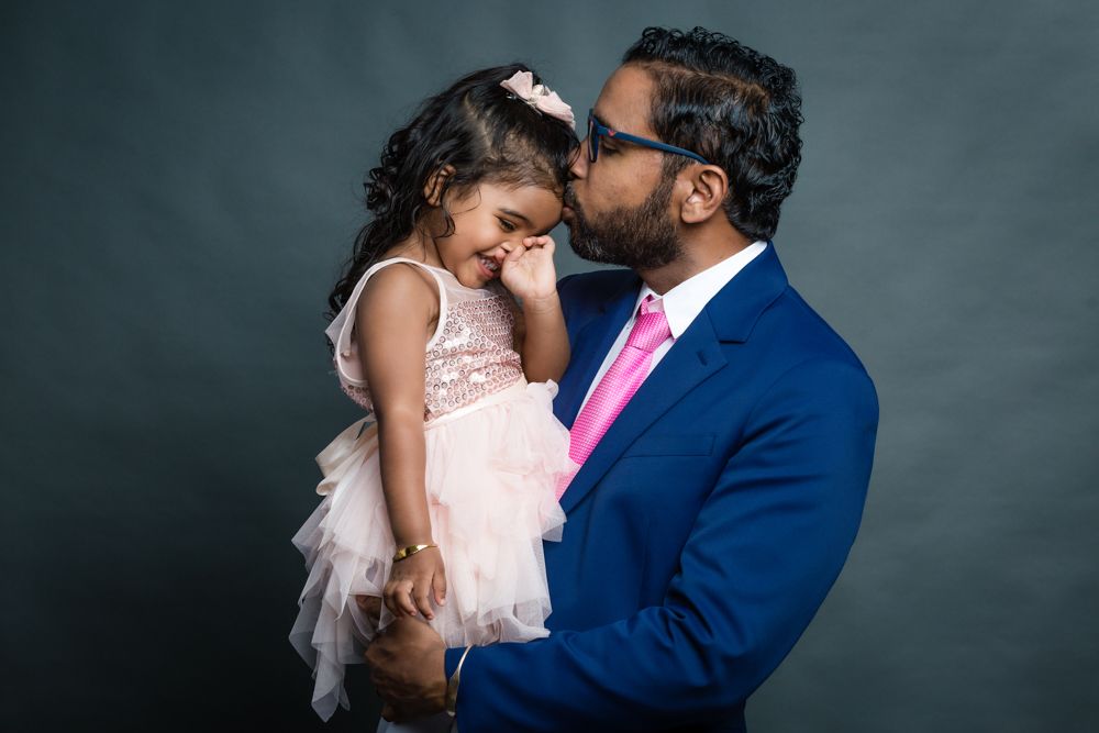 A tender moment between two people in formal attire, with a navy suit and pink tie against a dark backdrop.