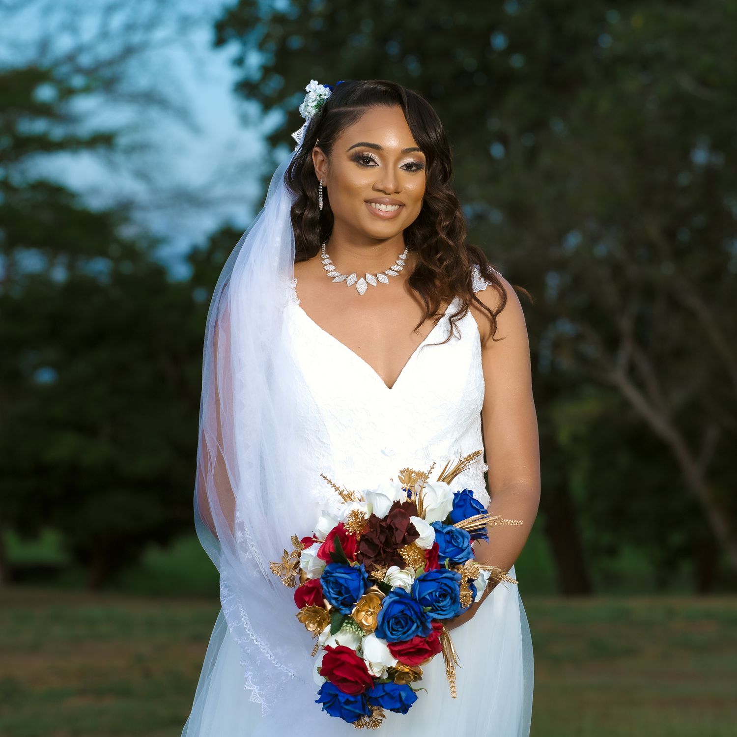 Bride holding red and blue bouquet poses in white V-neck wedding dress with flowing veil.