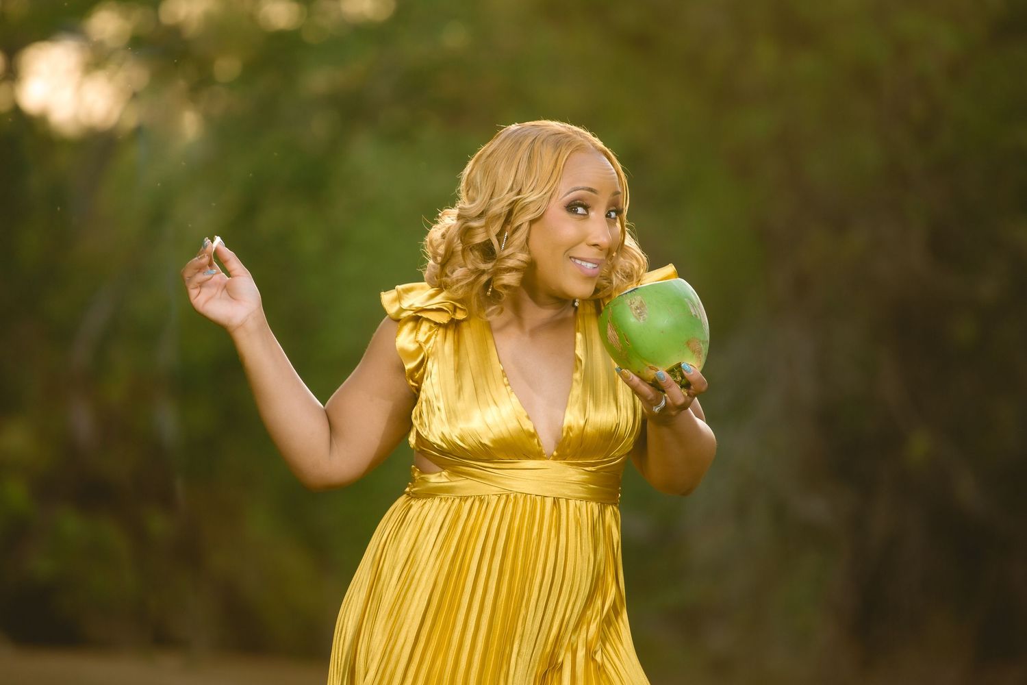 A person in a flowing yellow dress twirls in a sunlit outdoor setting with green grass and trees in the background.