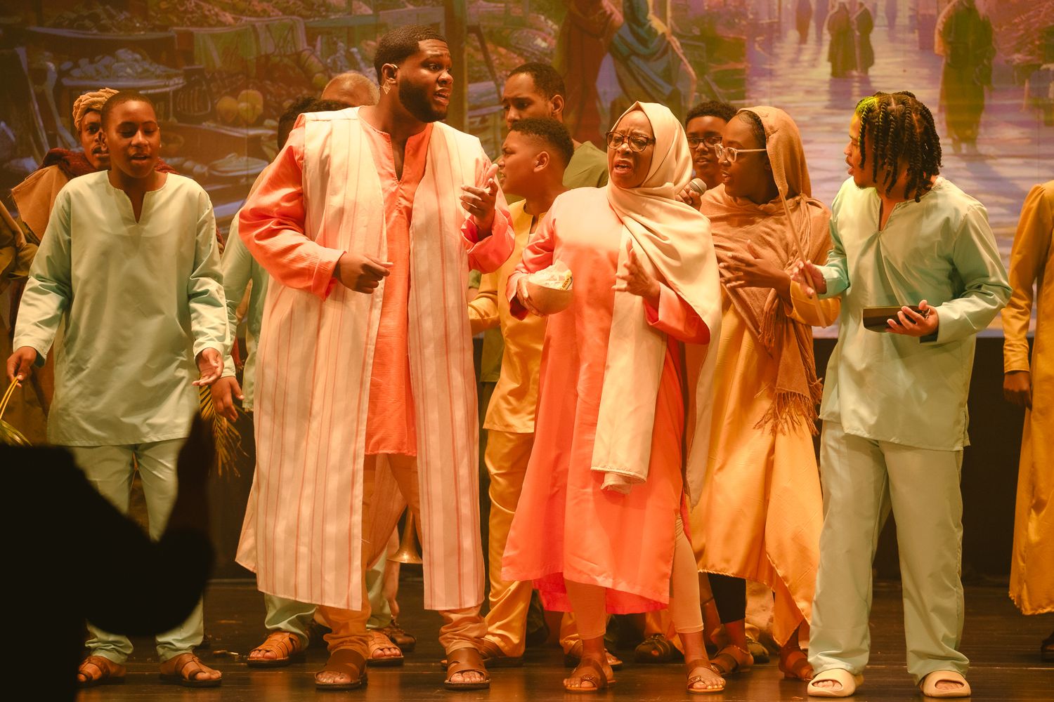 Group of performers in flowing orange and white robes performing on stage together.