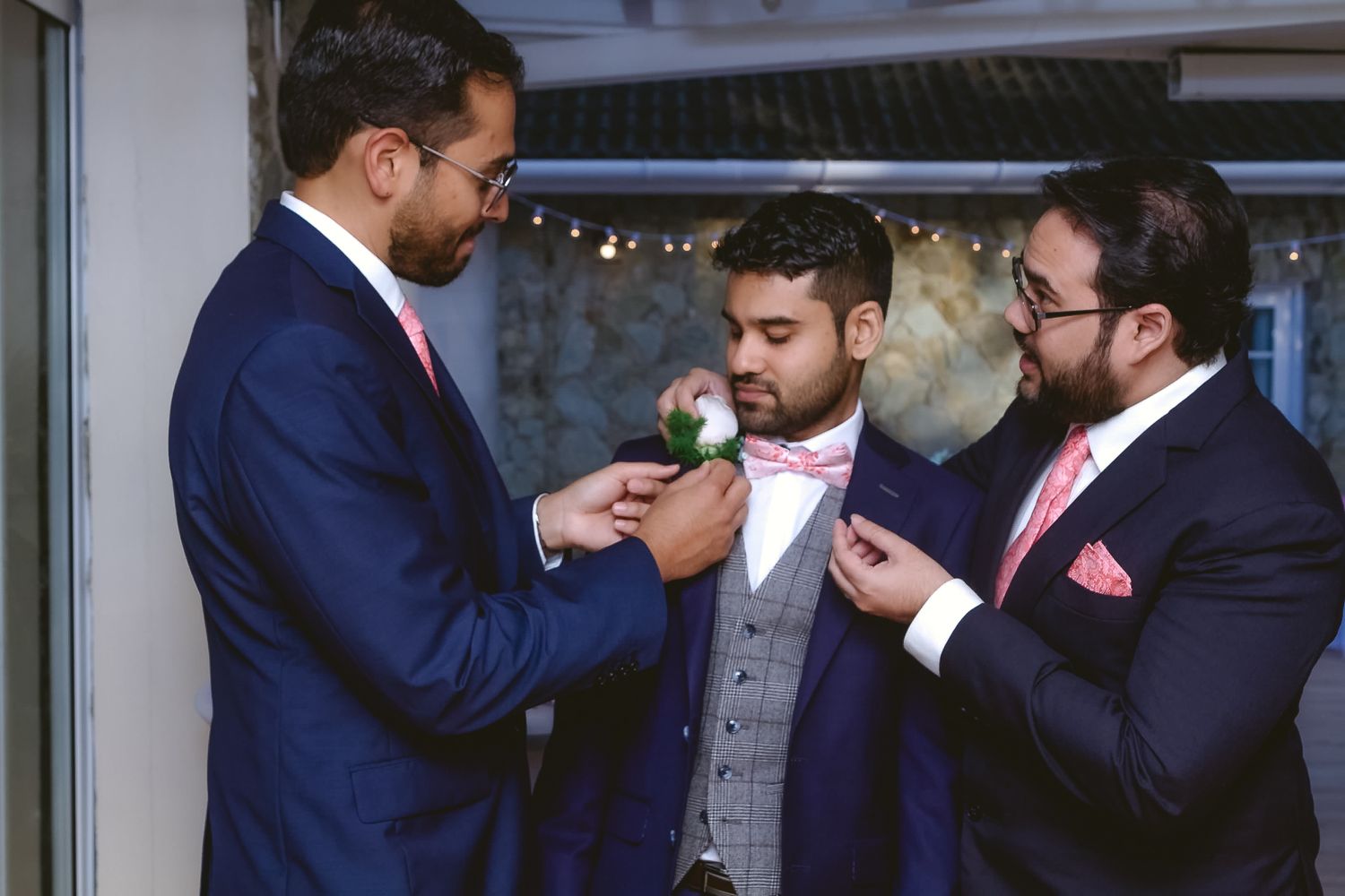 Three men in formal attire help adjust bowties before a special event.