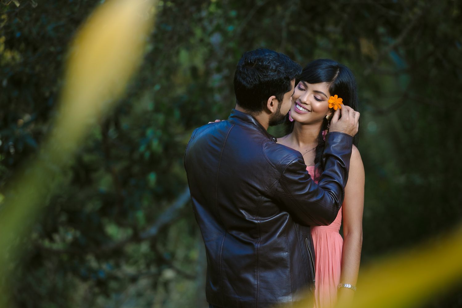 A romantic moment captured between a couple in a garden setting with soft natural lighting and blurred foliage.