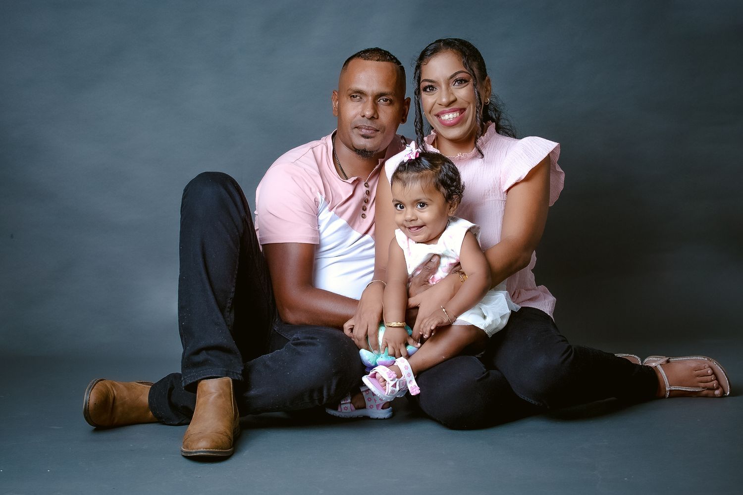 Family portrait with baby creating heartwarming moment against gray studio background.