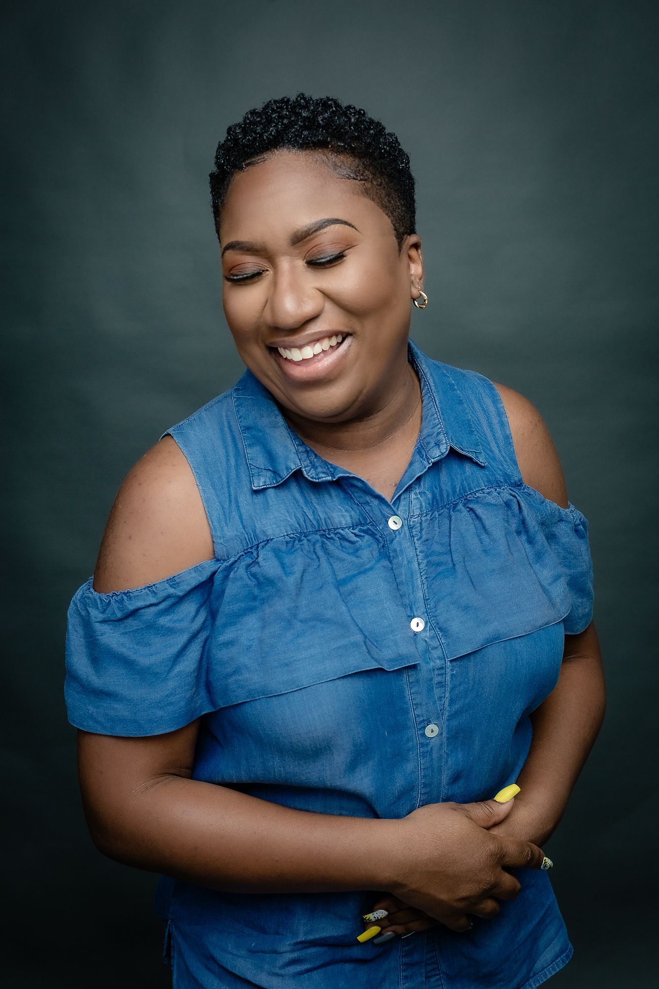 Candid portrait in blue denim top showing genuine smile against studio backdrop.