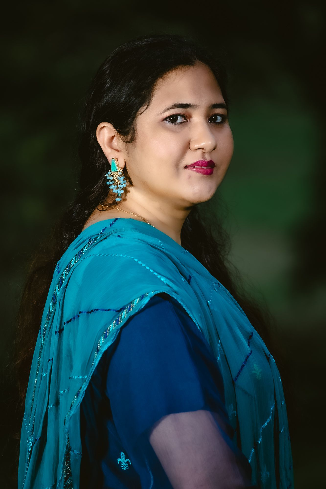 Portrait in traditional blue and teal sari with ornate turquoise earrings.