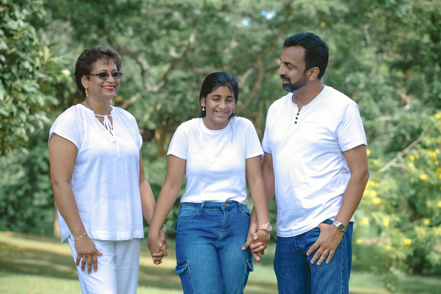 Three people in casual white and denim outfits stand together during an outdoor photo session.