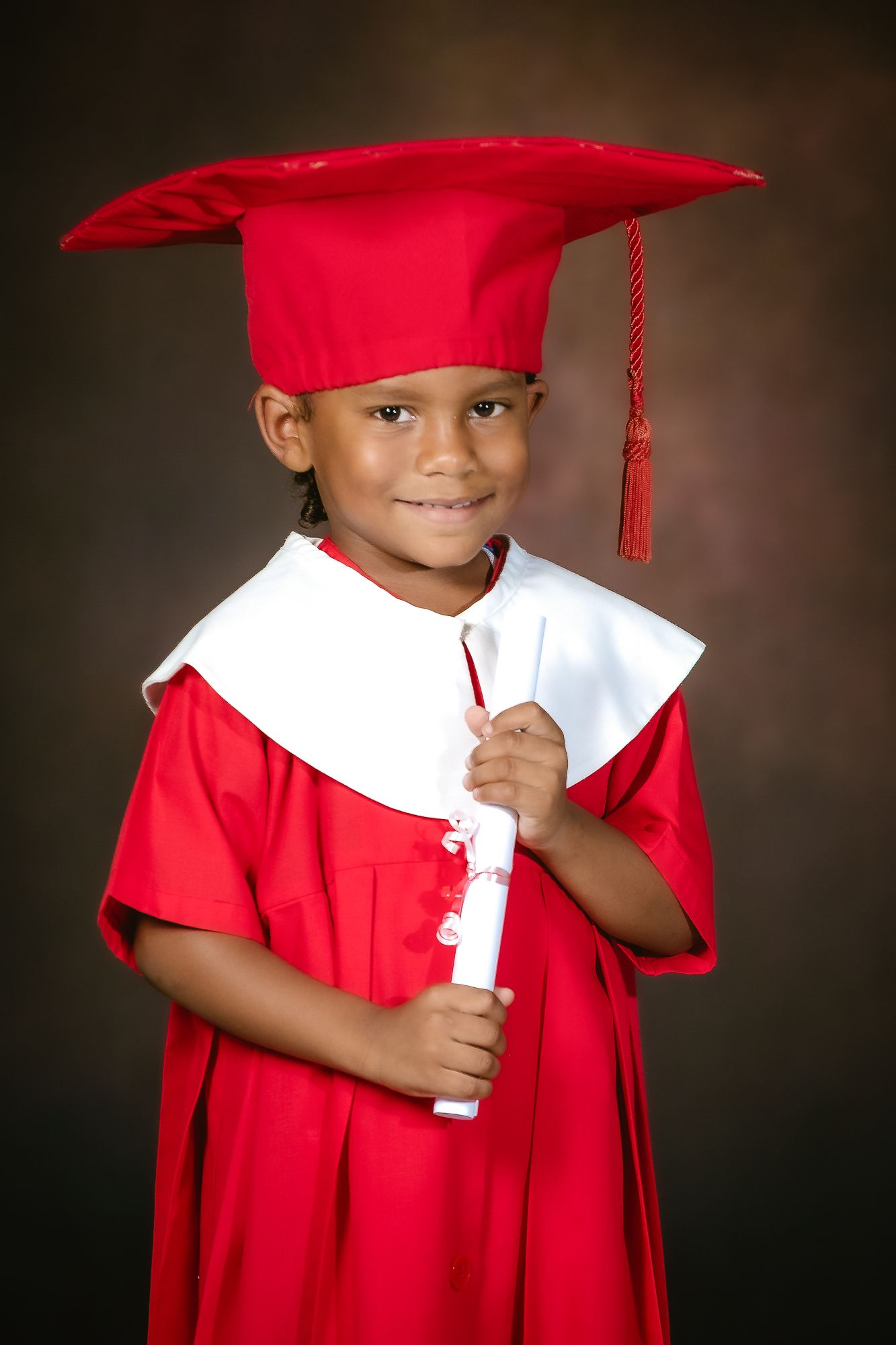 Young student wearing red graduation cap and gown smiles while holding diploma certificate.