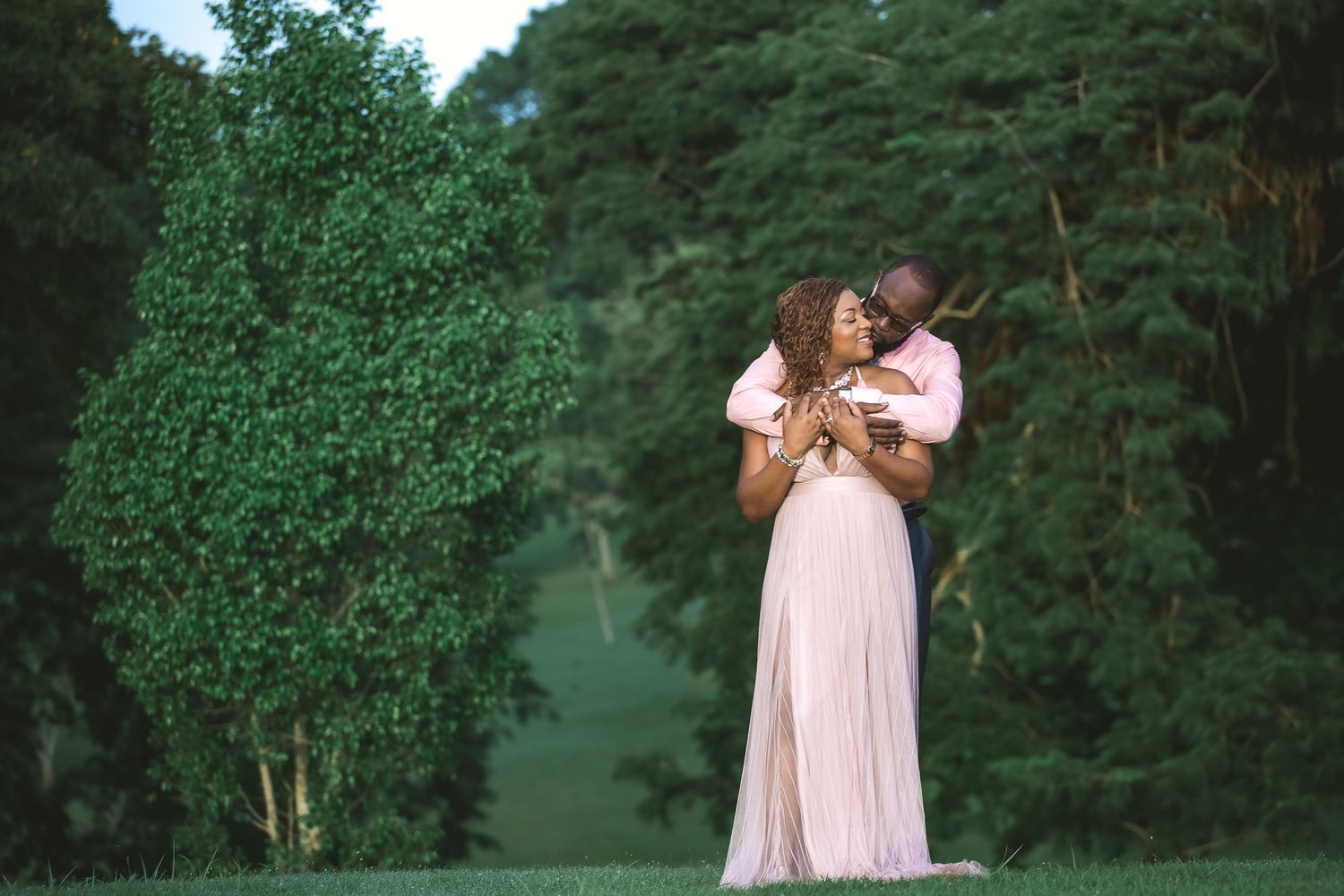 Tender outdoor portrait in pink dress against lush green foliage.