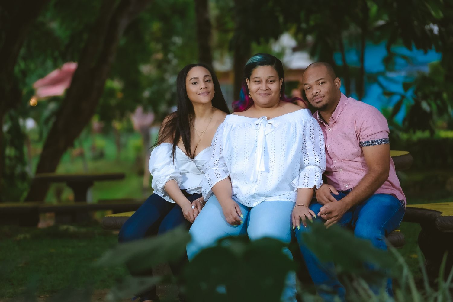 Three people sitting close together on bench in lush garden setting.