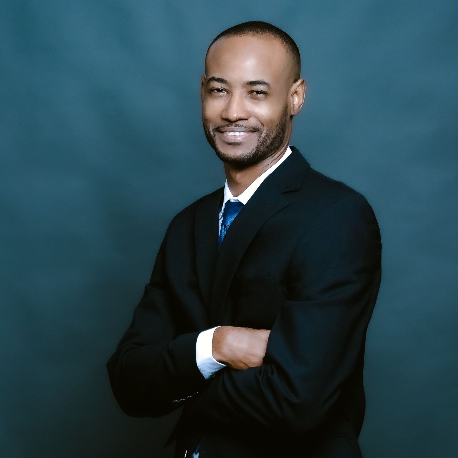 Professional headshot of person in dark suit with blue tie against blue background.