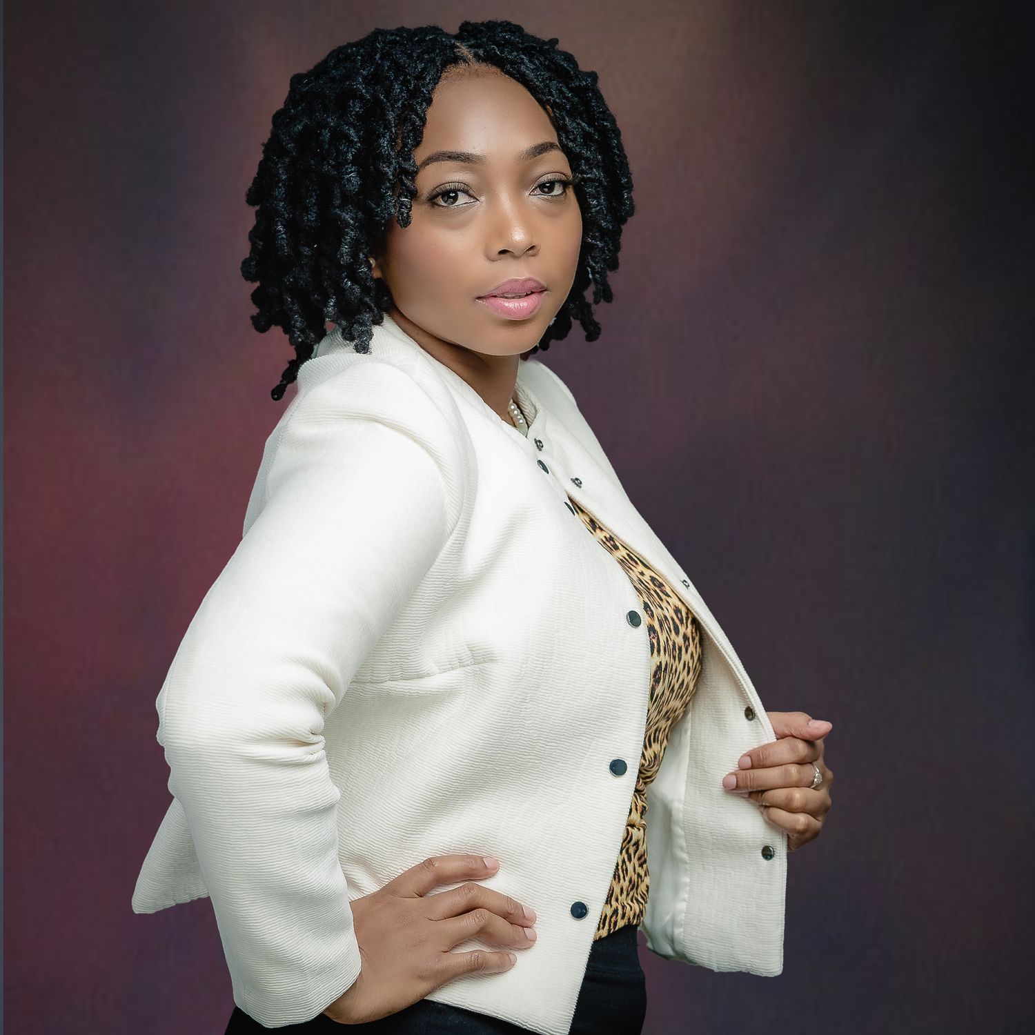 Professional headshot in white blazer and animal print top against warm background.
