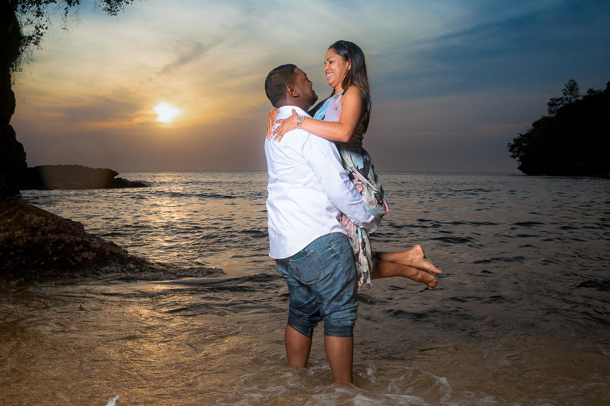 A romantic beach sunset scene with a couple embracing on the shoreline as golden light illuminates the ocean waves. Macqueripe, Trinidad
