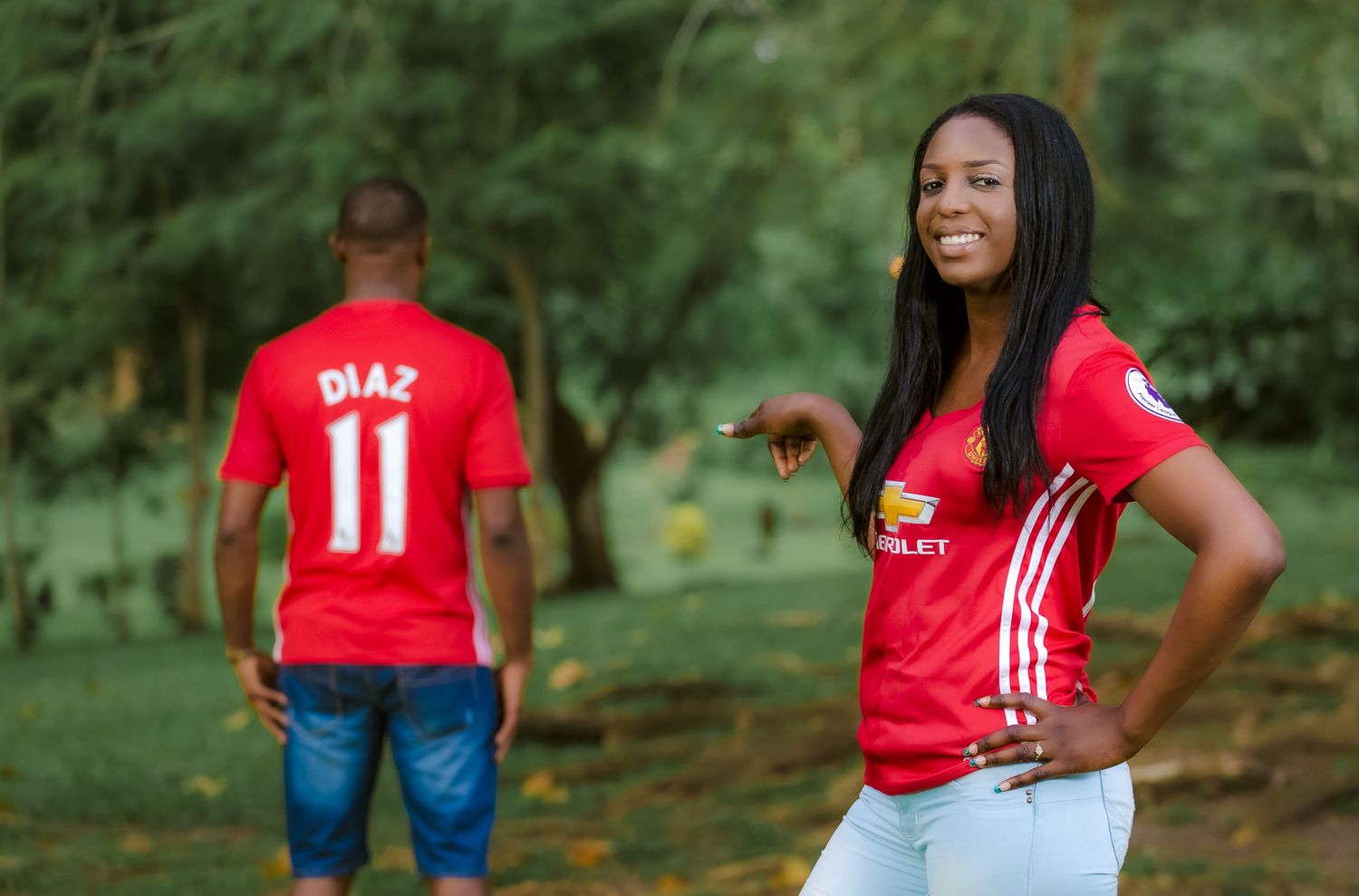 Two Manchester United fans pose in red jerseys outdoors, with number 11 jersey shown in background.
