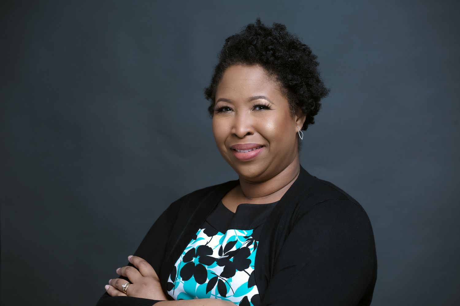 Professional headshot of person wearing black cardigan and patterned top against blue background.