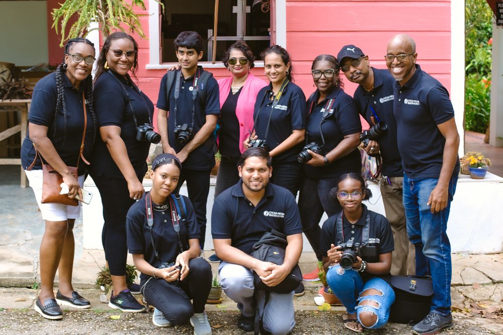Team members wearing matching navy uniforms gather for a group photo by a pink wall.