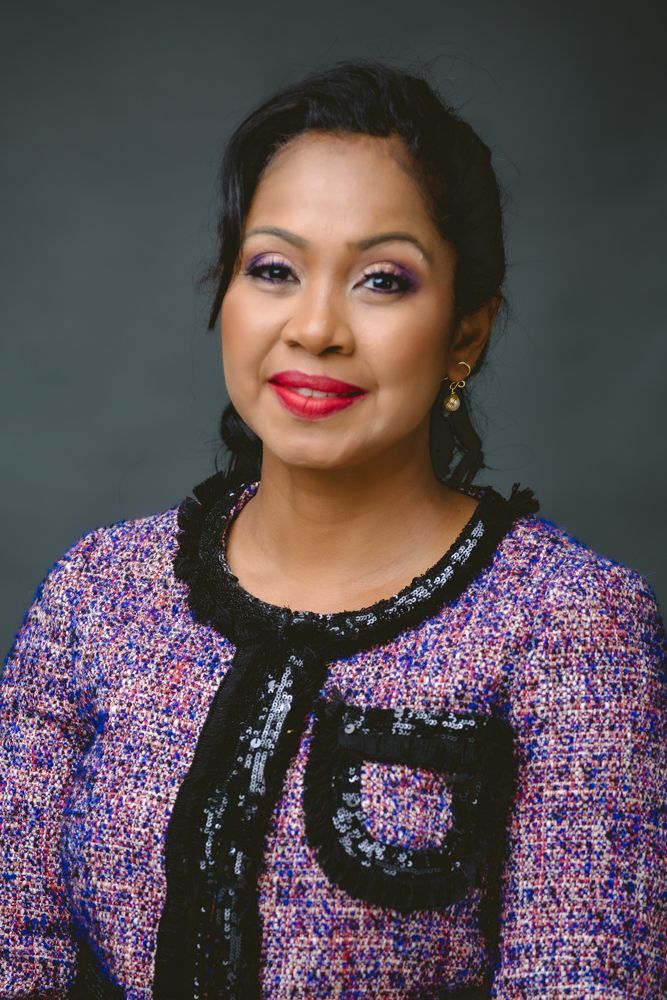 Professional portrait of someone wearing a purple tweed jacket with black trim and red lipstick against a dark background.