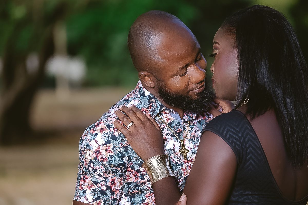 A romantic couple shares an intimate moment outdoors while wearing a floral shirt and black dress.