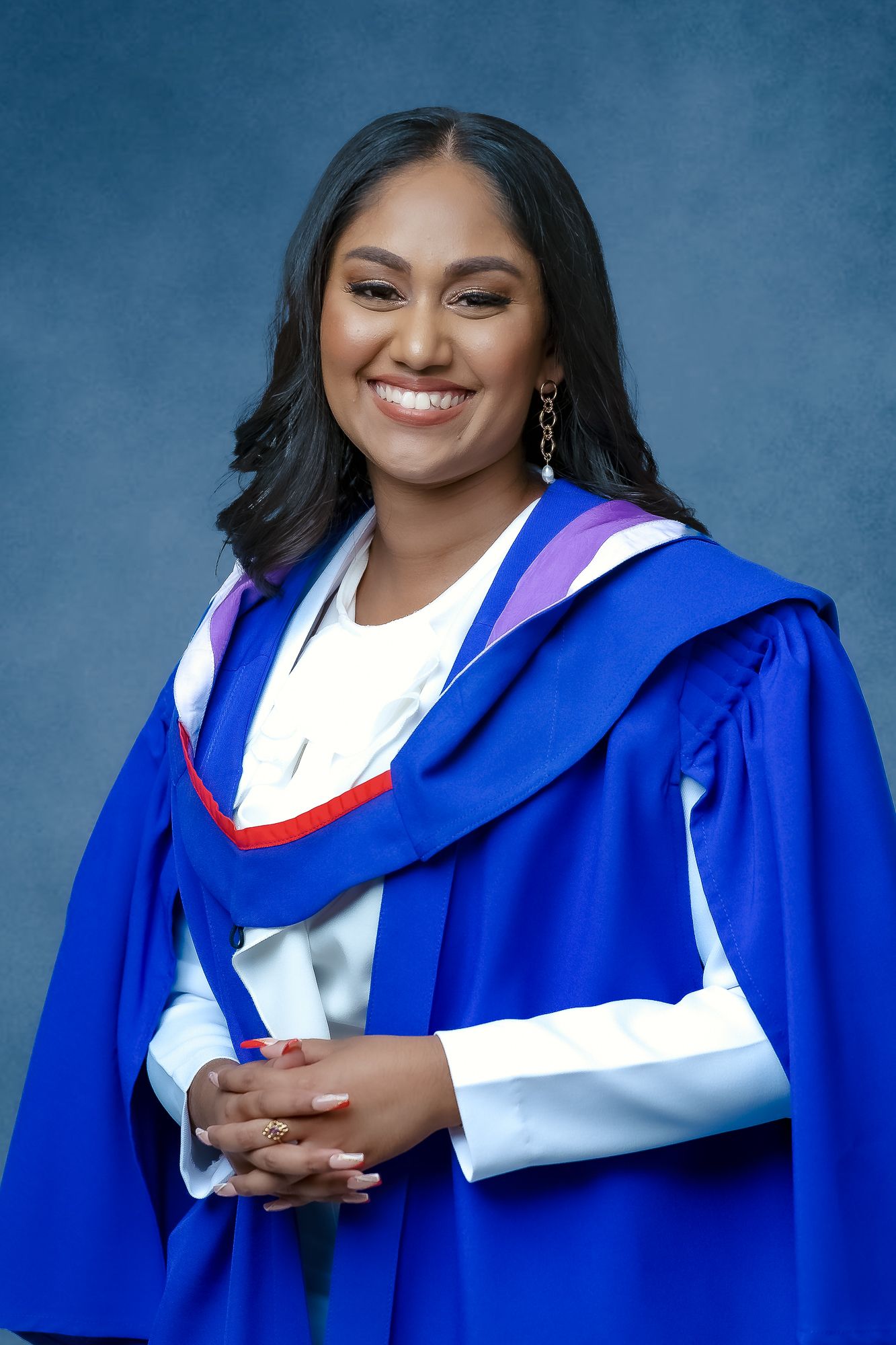 Graduate wearing blue and white academic regalia smiles warmly in formal portrait.