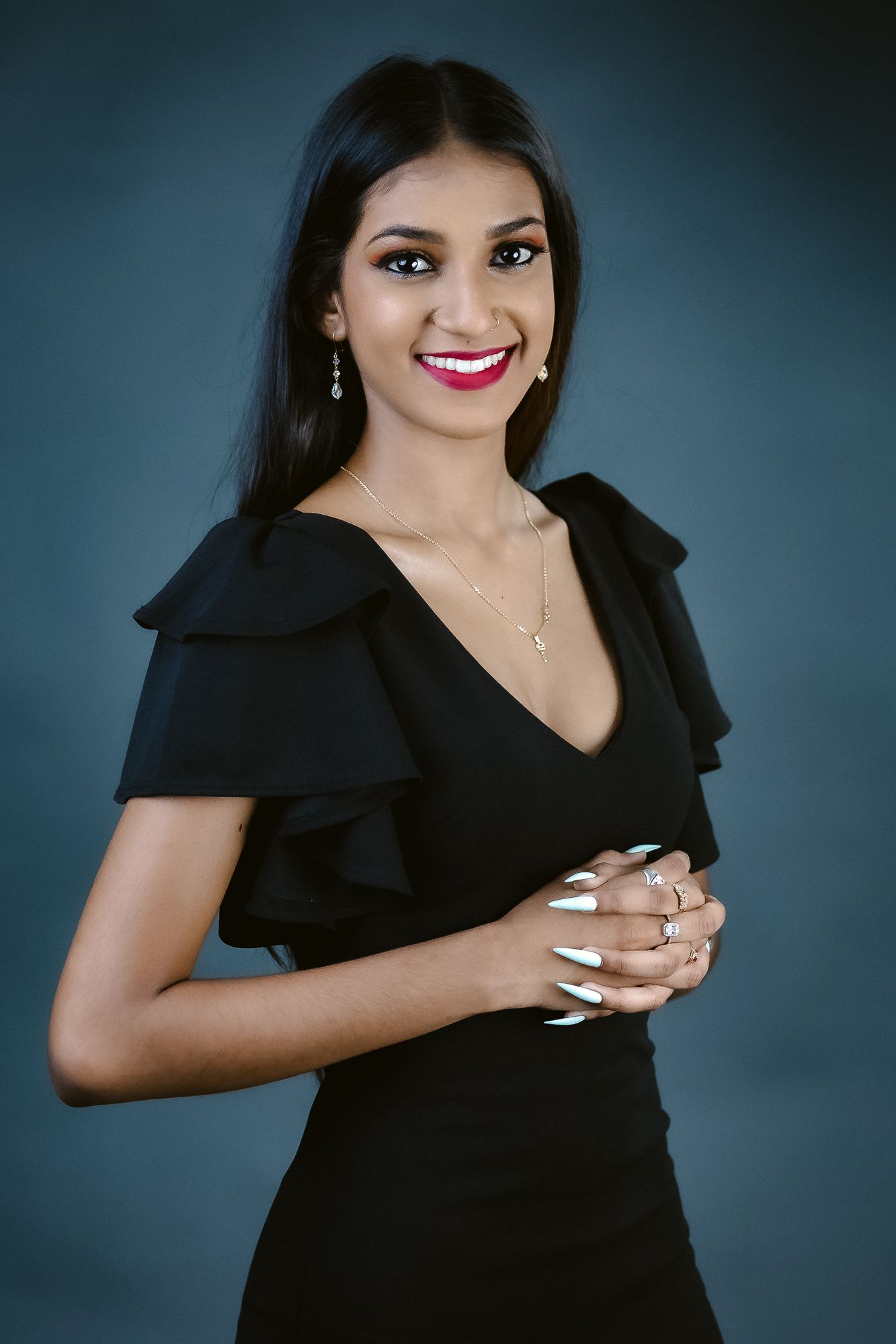 Person in black ruffled dress poses elegantly against dark studio background.
